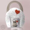 Set de taza blanca con gatito gruñón sosteniendo un corazón rojo y frase “Los odio a todos”, acompañado de porta taza con diseño de confetti y corazón rojo, ideal como regalo divertido y original.