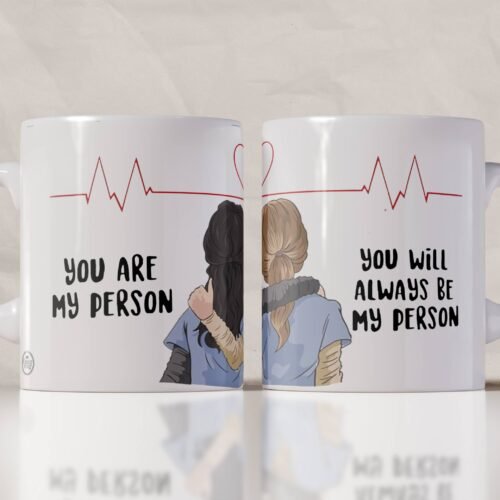 Taza blanca inspirada en Grey’s Anatomy con ilustración de dos amigas abrazadas, línea de electrocardiograma en forma de corazón y frase “You are my person / You will always be my person”